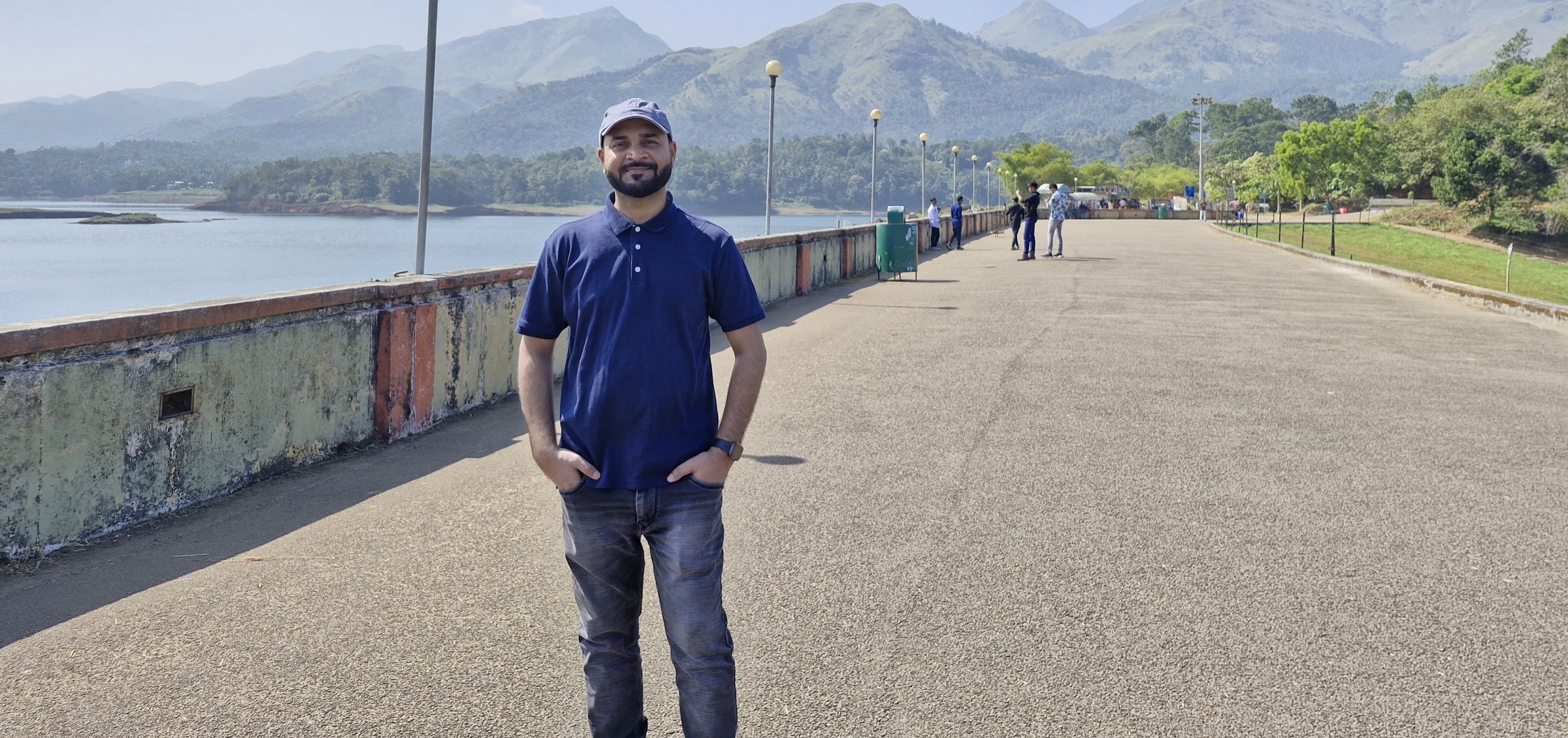Rajan Kumar standing on a dam walkway with hills behind him
